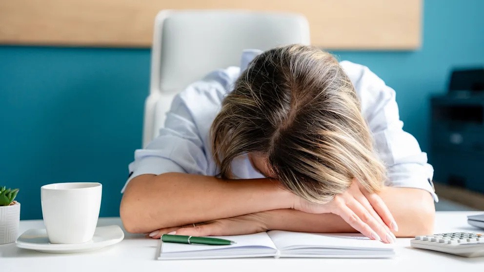 Eine erschöpfte Person liegt mit dem Kopf auf dem Schreibtisch